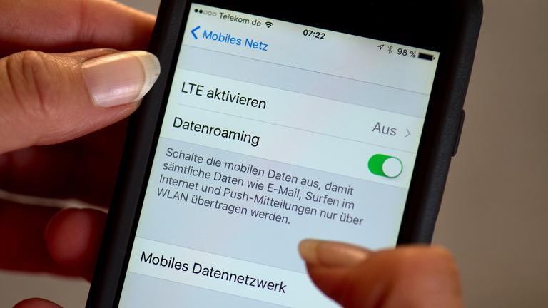 Eine Hand hält ein Smartphone. Darauf sind die Einstellungen für das Datenroaming und mobile Daten zu sehen.