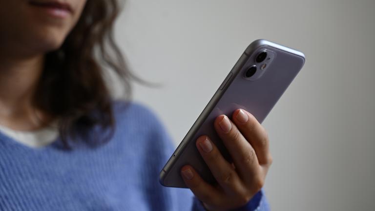 Eine Frau in einem blauen Pullover hält ein Smartphone in der Hand.