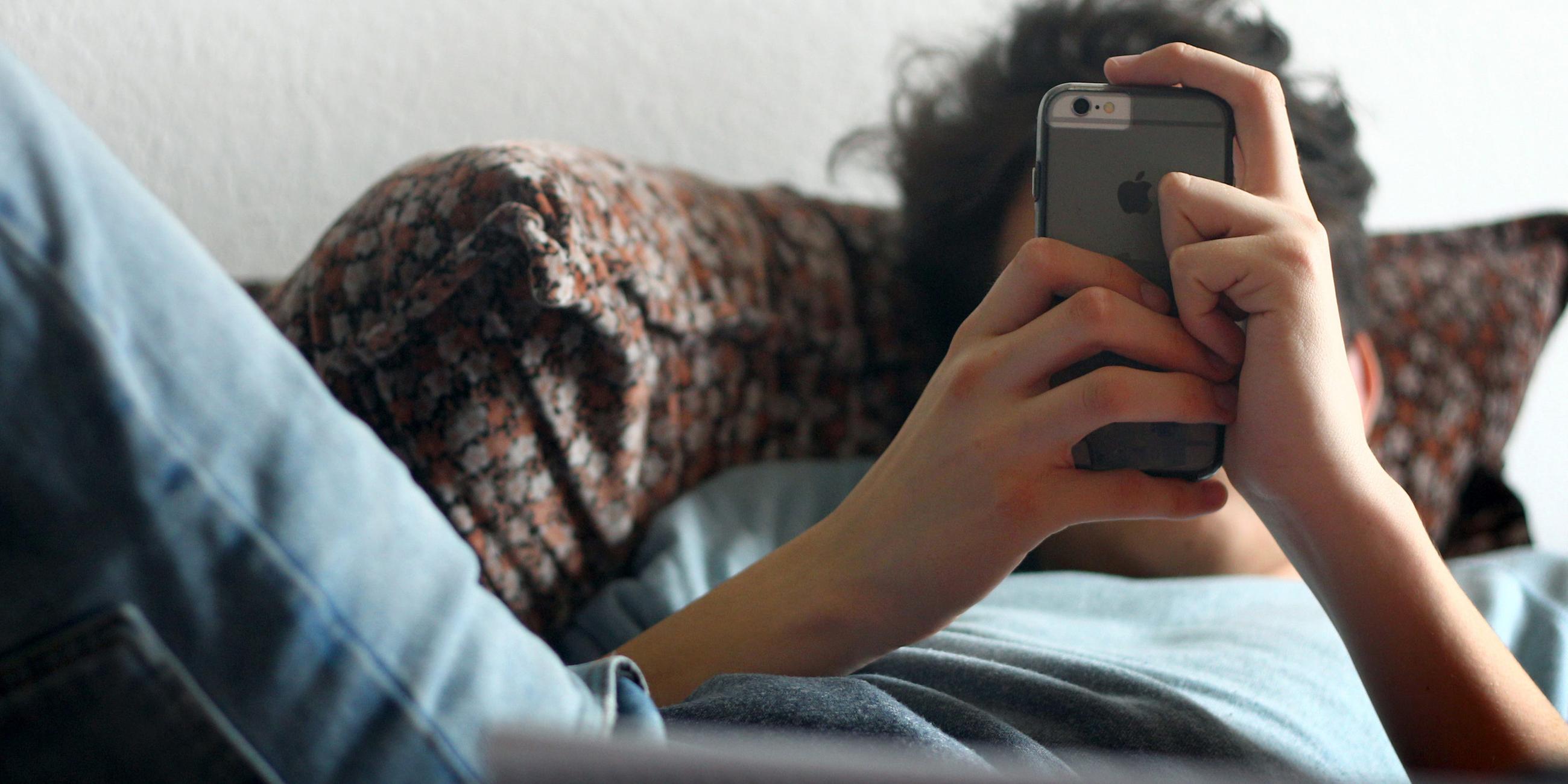 Archiv: Ein junger Mann mit seinem Smartphone vor der Couch
