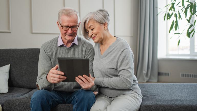 Ein älteres Paar sitzt mit einem Tablet auf dem Sofa.