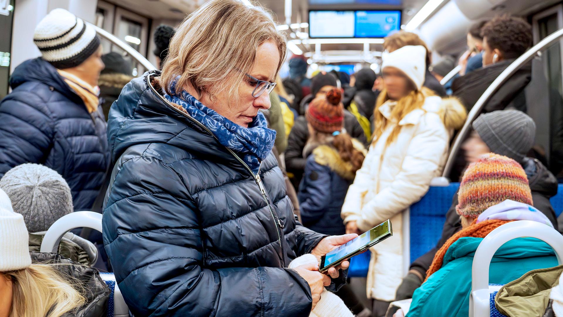 Frau liest Nachrichten auf ihrem Smartphone, in der vollbesetzten U-Bahn