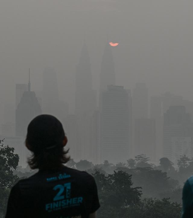 Menschen betrachten am Morgen des 17. Oktober 2026 bei Sonnenaufgang die dunstverhangene Skyline von Kuala Lumpur, während das Land weiterhin in einen Dunst gehüllt ist, der durch Brände in Indonesien verursacht wurde.