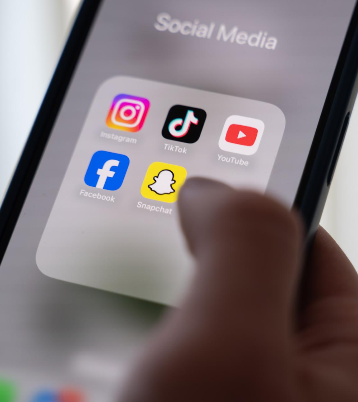 Eine Person hält ein Smartphone, auf dessen Display verschiedene Social Media Apps angezeigt werden.