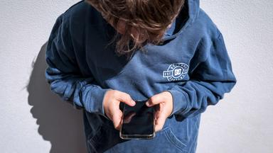 Jugendlicher Australier schaut auf sein Handy