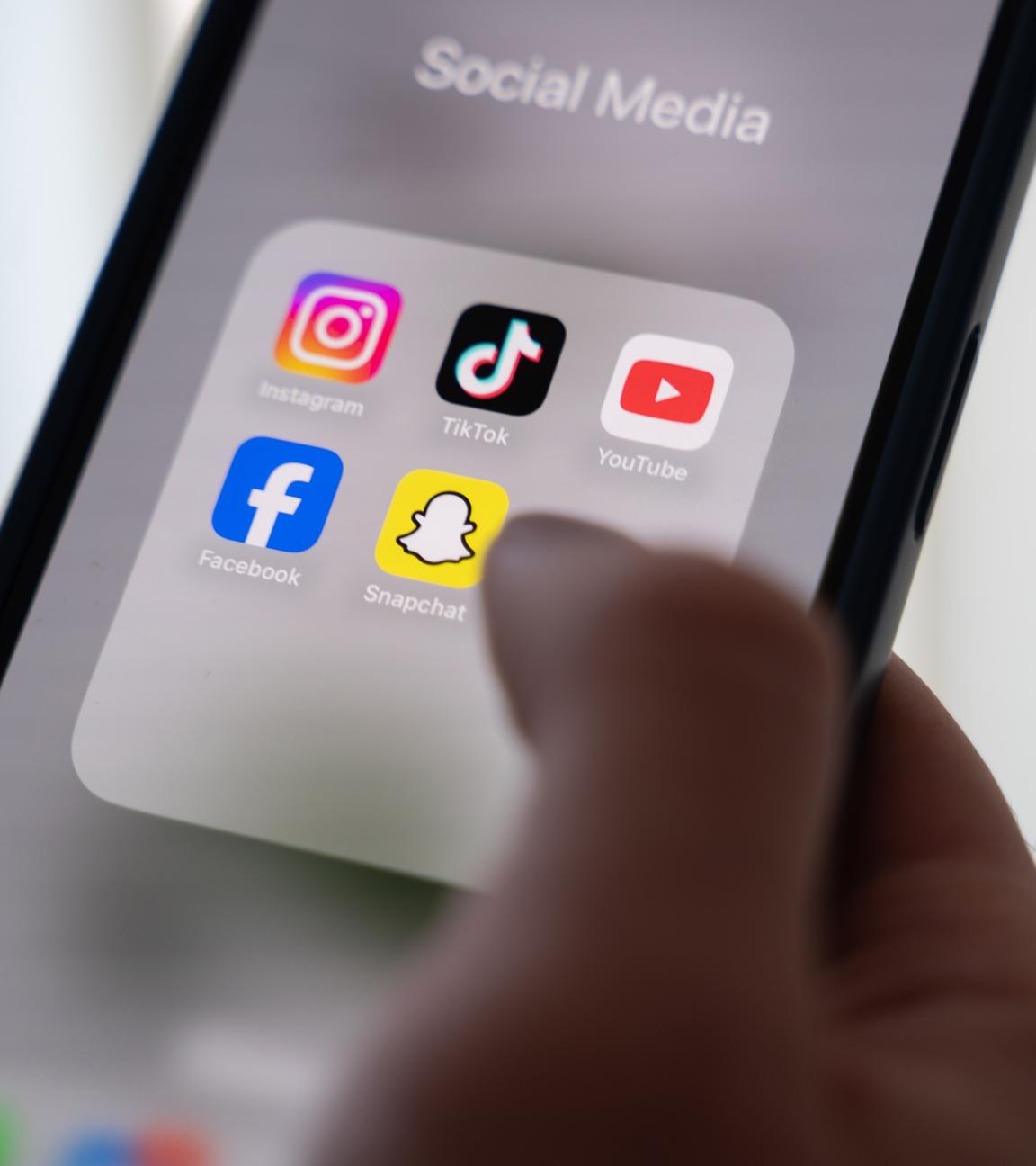 Eine Frau hält ein Smartphone, auf dessen Display verschiedene Social Media Apps angezeigt werden.