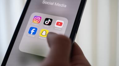 Eine Frau hält ein Smartphone, auf dessen Display verschiedene Social Media Apps angezeigt werden.