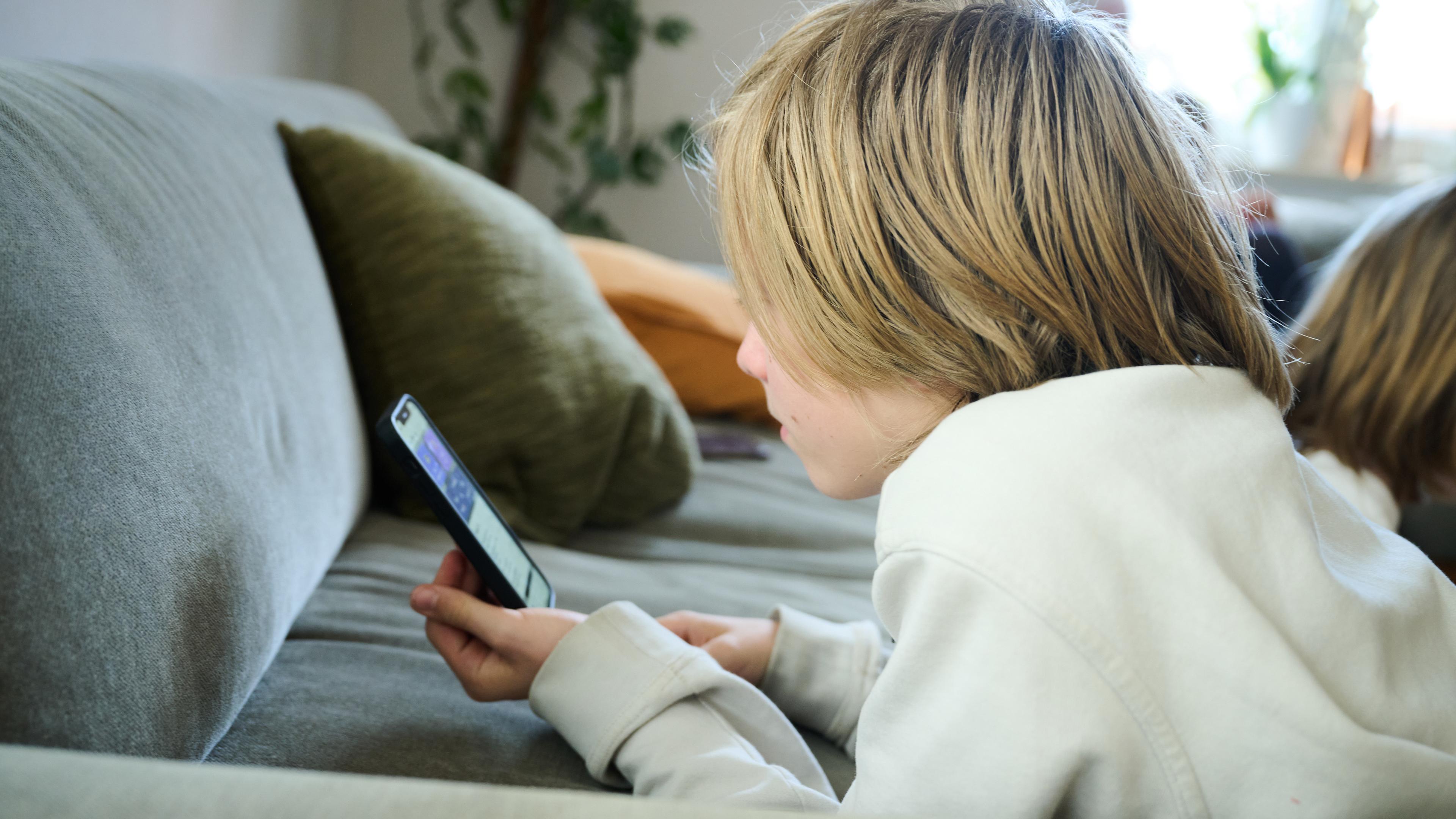 Ein Kind liegt auf dem Sofa und schaut auf ein Handy
