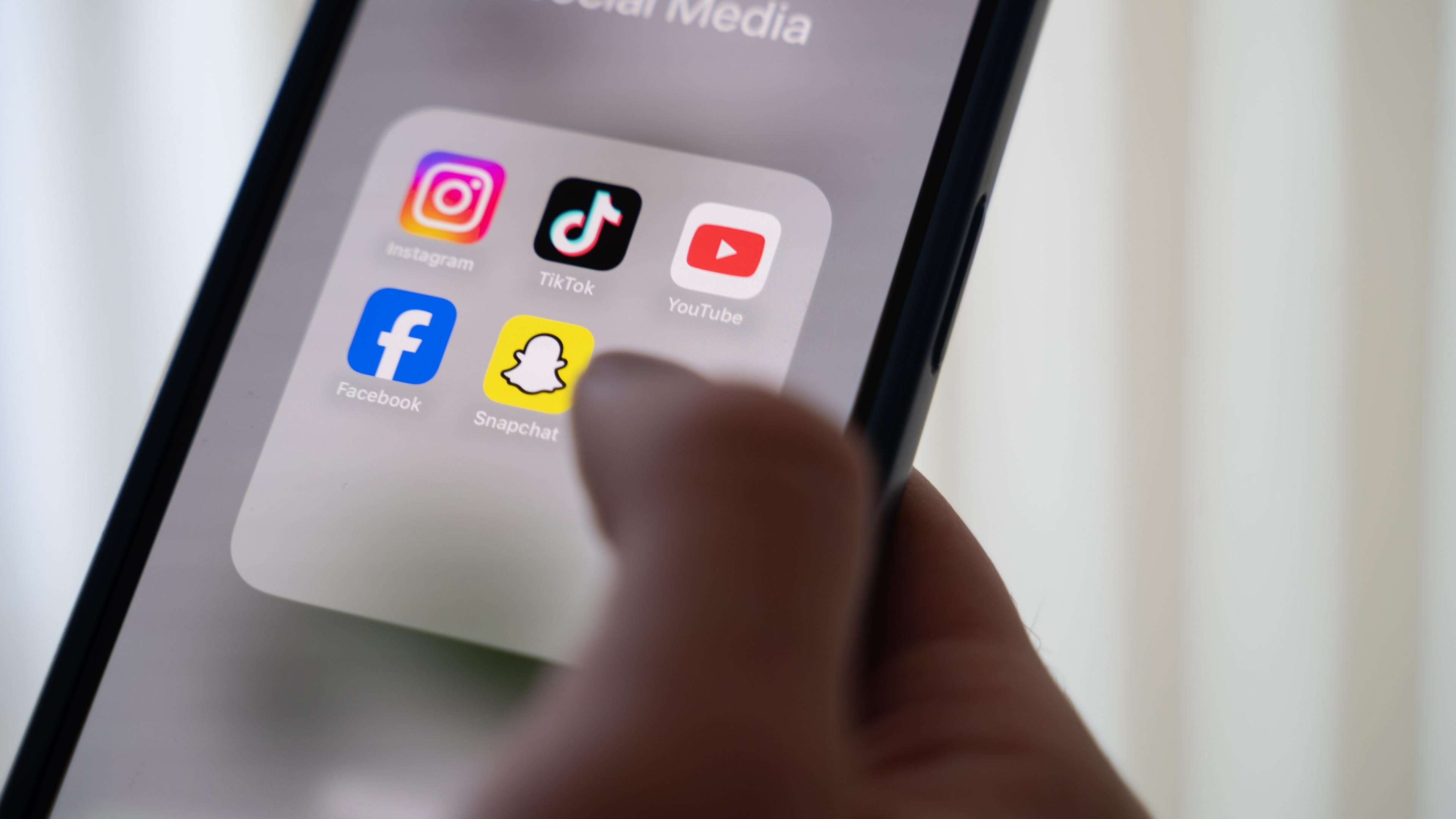 Eine Person hält ein Smartphone, auf dessen Display verschiedene Social Media Apps angezeigt werden.