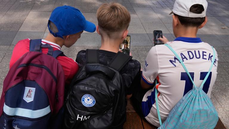 Symbolbild: Hugo W., (r-l), Hardy M. und Edan A., alle 11 Jahre alt, benutzen ihre Telefone, während sie vor einer Schule in Sydney sitzen.