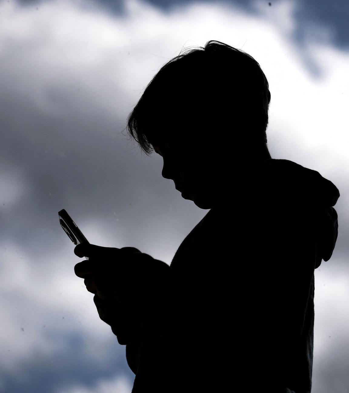 Den Schatten eines Jungen mit Handy in der Hand. Im Hintergund ist ein wolkenverhangener Himmel