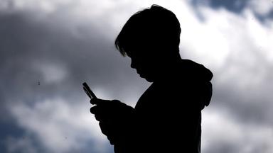 Den Schatten eines Jungen mit Handy in der Hand. Im Hintergund ist ein wolkenverhangener Himmel