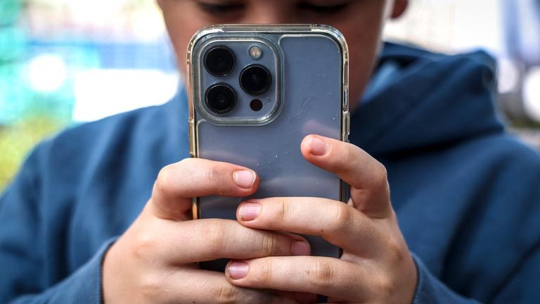 Ein Junge schaut auf sein Handy. Das Handy ist im Vordergrund, sodass sein Gesicht fast nicht zu sehen ist.