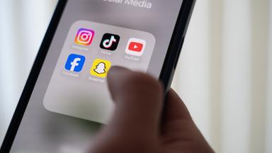  Eine Frau hält ein Smartphone, auf dessen Display verschiedene Social Media Apps angezeigt werden. 