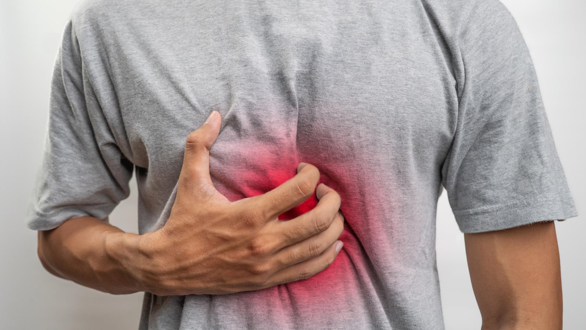 Mann spürt Brennen in der Mitte der Brust und hält eine Hand darauf.