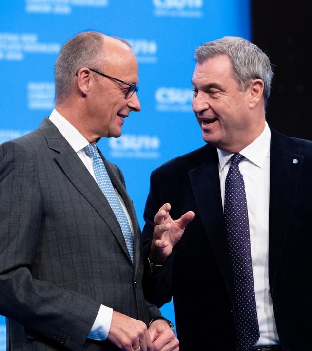 Das Bild zeigt CSU-Chef Söder (r.) und Bundeskanzler Merz (CDU) beim CSU-Parteitag, wie sie miteinander sprechen.