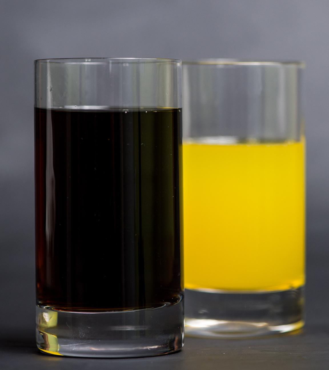 Ein Glas mit Cola steht neben einem Glas mit Orangenlimonade.
