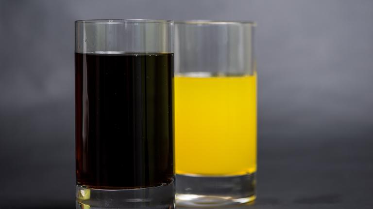 Ein Glas mit Cola steht neben einem Glas mit Orangenlimonade.