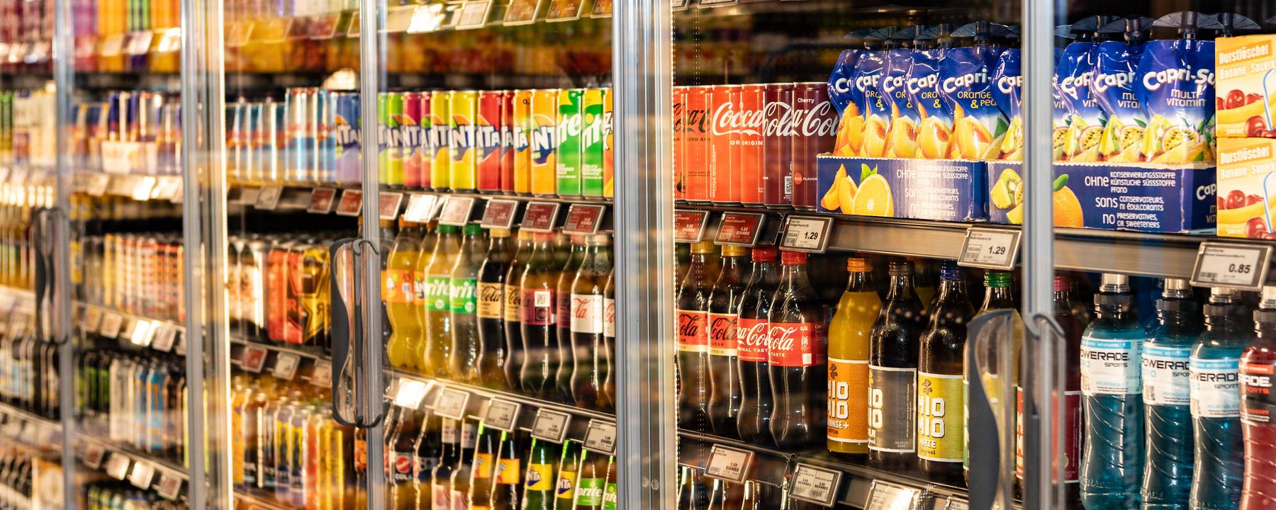 Ein Kühlregal mit unterschiedlichen Softdrinks, darunter, Capri-Sonne, Coca Cola, Fanta, Sprite, Mezo-Mix und Vitrex. 