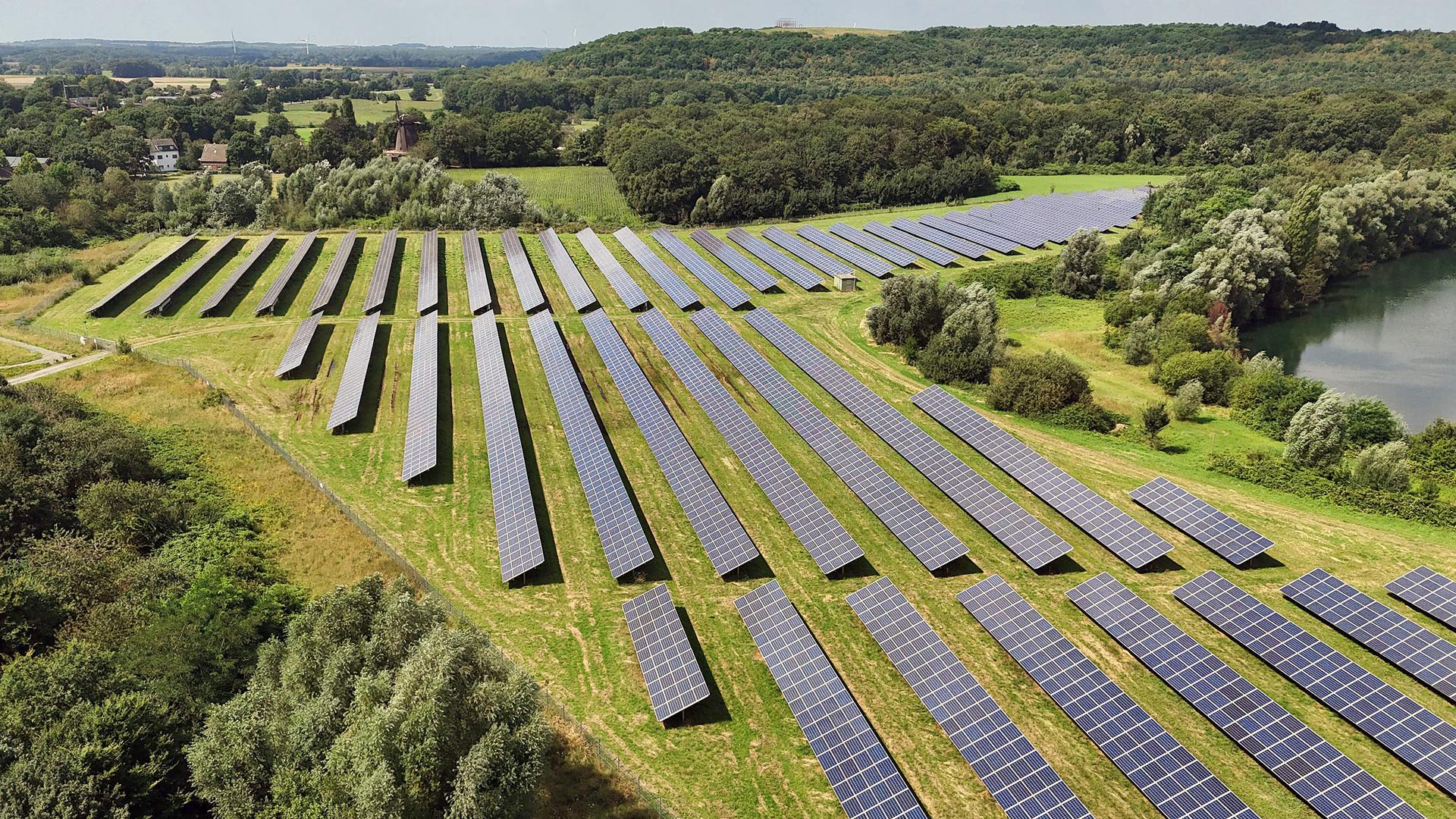 Sonnenkollektoren auf einem Solarfeld vor einem See in Neukirchen-Vluyn