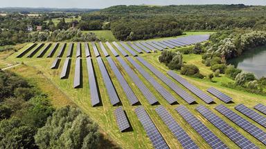 Sonnenkollektoren auf einem Solarfeld vor einem See in Neukirchen-Vluyn