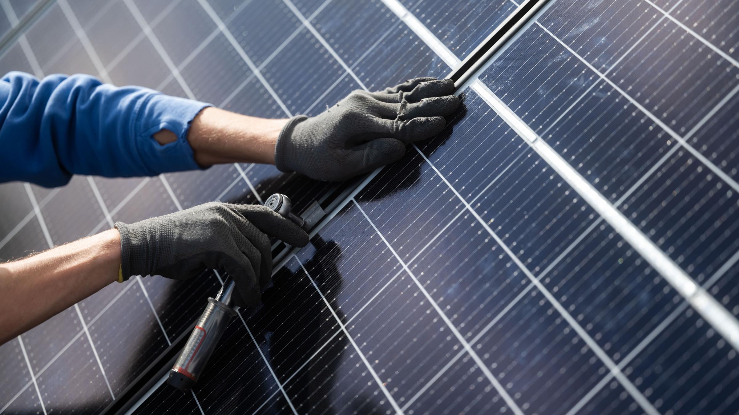 Ein Mann montiert Photovoltaikmodule auf dem Dach eines Wohnhauses.