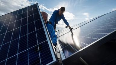 Mitarbeiter einer Firma montieren Photovoltaikmodule auf dem Dach eines Wohnhauses.