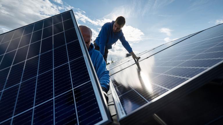 Mitarbeiter einer Firma montieren Photovoltaikmodule auf dem Dach eines Wohnhauses.