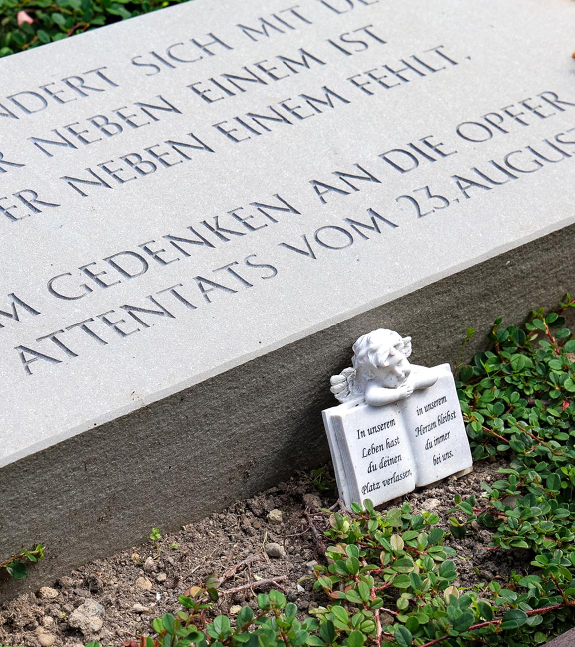 Ein Gedenkstein und Kerzen liegen auf einer Grünfläche am Fronhof zum Gedenken der Opfer ein Jahr nach dem Terroranschlag von Solingen.