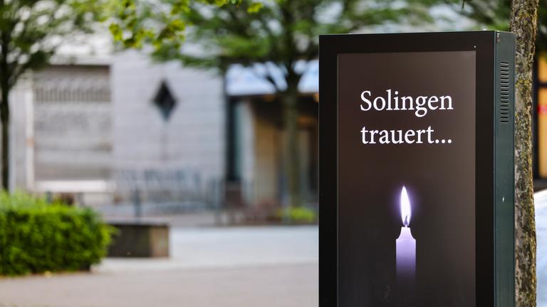 Solingen: Am Fronhof, dem Tatort des Messeranschlags von Solingen, steht der Schriftzug "Solingen trauert" und eine Kerze auf einem Bildschirm. 