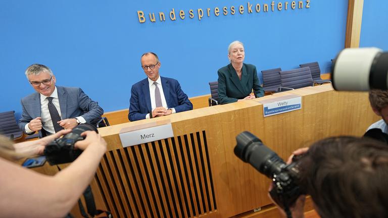Bundeskanzler Friedrich Merz (CDU, M) sitzt mit Stefan Kornelius, Sprecher der Bundesregierung, und der Journalistin Ute Welty, die die Pressekonferenz leitet, bei seiner Sommer-Pressekonferenz in der Bundespressekonferenz. 