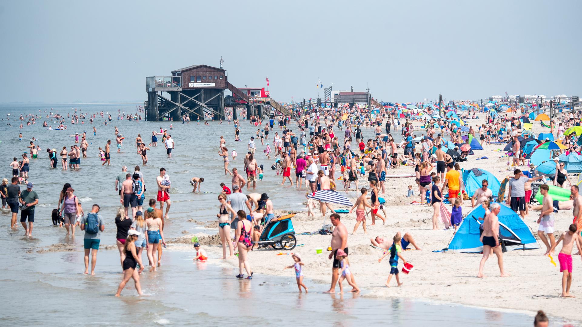 Schleswig-Holstein, Sankt Peter-Ording: Zahlreiche Touristen sind bei Sonnenschein am Strand an der Nordsee unterwegs.