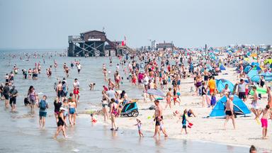 Schleswig-Holstein, Sankt Peter-Ording: Zahlreiche Touristen sind bei Sonnenschein am Strand an der Nordsee unterwegs.