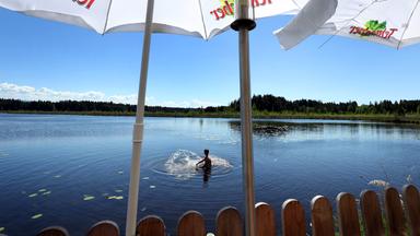Ein junger Mann sucht hinter den Sonnenschirmen eines Ausflugslokales Abkühlung im Elbsee.