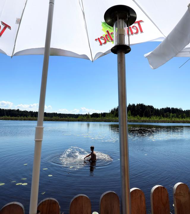 Ein junger Mann sucht hinter den Sonnenschirmen eines Ausflugslokales Abkühlung im Elbsee.