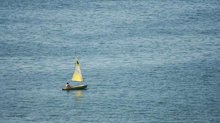 Baden-Württemberg, Überlingen: Ein Mann segelt mit einem kleinen Segelboot auf dem Bodensee bei Überlingen. Nach der Hitze werden am Wochenende teilweise Gewitter und Starkregen erwartet.