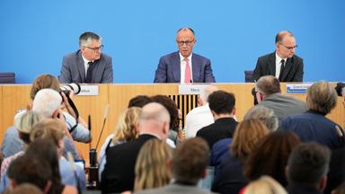 Bundeskanzler Friedrich Merz bei der Sommerpresssekonferenz. Im Vordergrund Journalisten, die Fragen stellen.