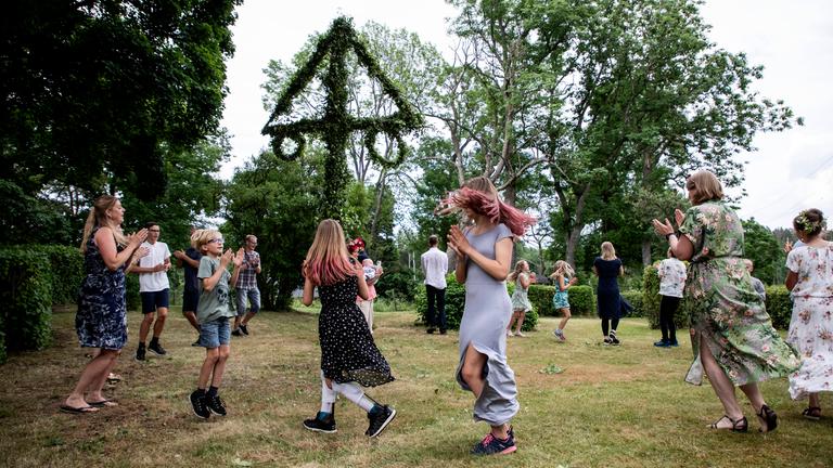 Feiernde tanzen um Mittsommerbaum in Schweden
