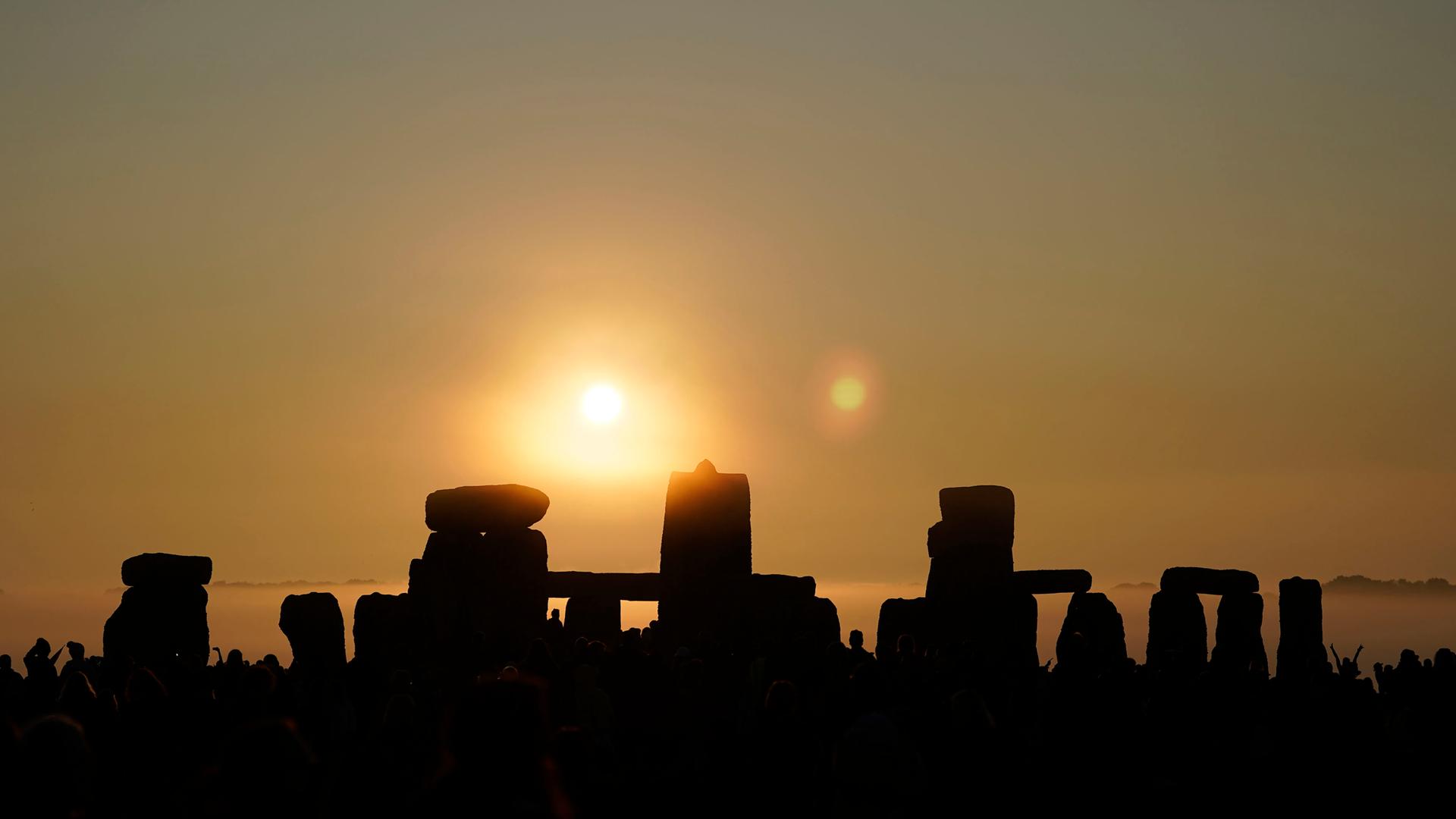 Menschen versammeln sich bei Sonnenaufgang um den Heel Stone, am Tag der Sommersonnenwende in Stonehenge. 