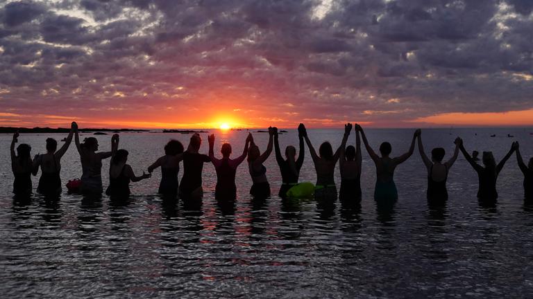 An der Cullercoats Bay in North Tyneside, Großbritannien versammeln sich Menschen bei Sonnenaufgang zur Sommersonnenwende, dem längsten Tag des Jahres, im Wasser. 