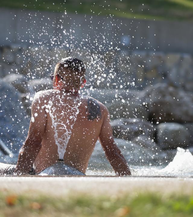 Ein Mann sitzt im Freibad unter einem Wasserspiel.