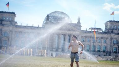 Ein Urlauber aus Irland erfrischt sich vor dem Reichstagsgebäude unter einem Rasen Sprenger bei hochsommerlichen Temperaturen am 19.06.2026 in Berlin.