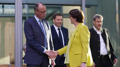 Friedrich Merz und Saskia Esken geben sich die Hand vor dem Marie-Elisabeth-Lüders-Haus. Im Hintergrund sind Lars Klingbeil und Markus Söder zu sehen.