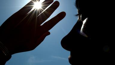 Eine Frau schützt sich mit einer erhobenen Hand vor der Sonne.