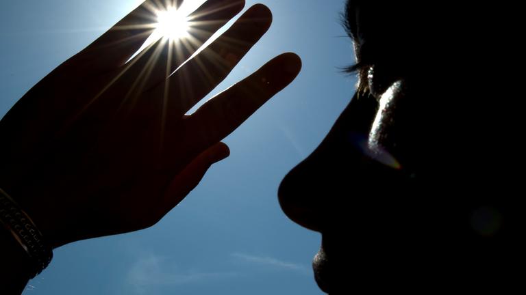 Eine Frau schützt sich mit einer erhobenen Hand vor der Sonne.
