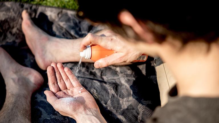Ein Mann sprüht Sonnencreme in seine Handfläche