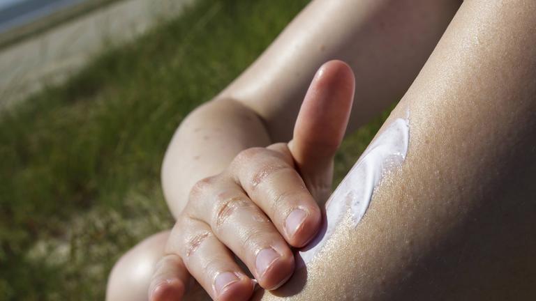 Eine Frau reibt sich den Arm mit Sonnencreme ein. 