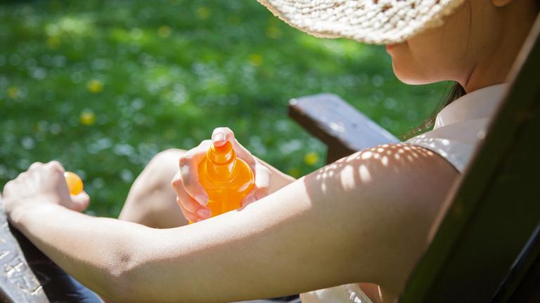 Symbolfoto:Eine Frau sprüht sich mit Sonnenschutz ein