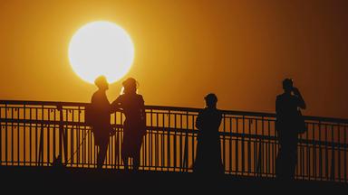 Personen zeichnen sich als Silhouette ab vor der untergehenden Sonne in Berlin am 19.06.2026.