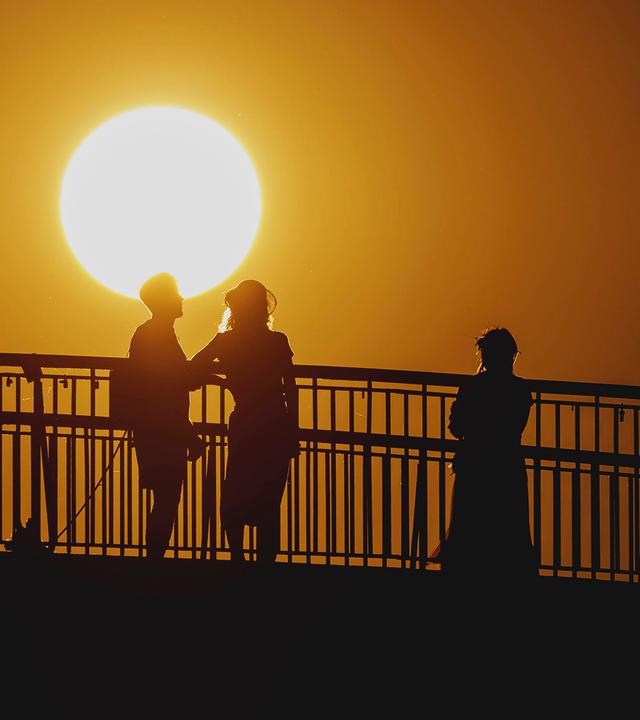 Personen zeichnen sich als Silhouette ab vor der untergehenden Sonne in Berlin am 19.06.2026.