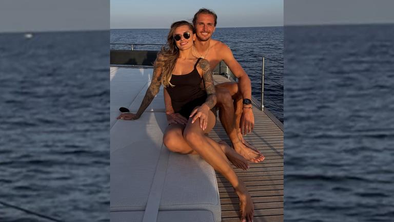 Sophia Thomalla (links) und Alexander Zverev sitzen auf einem Boot und lächeln in die Kamera.